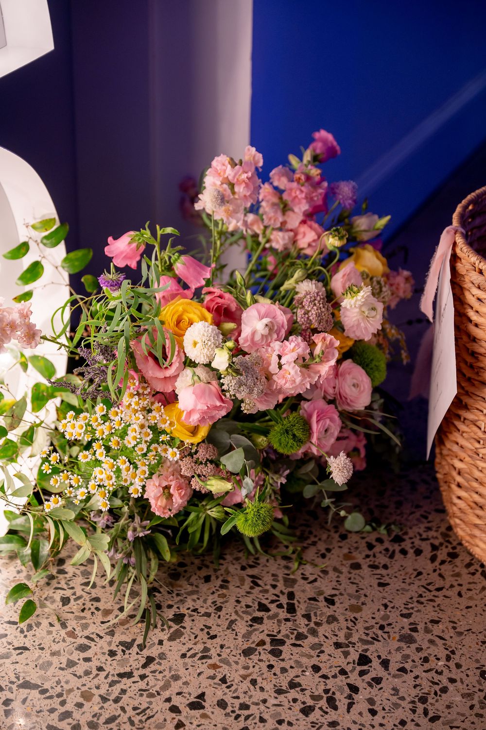 Lush floral arrangement with pink roses and mixed blooms against a blue wall.