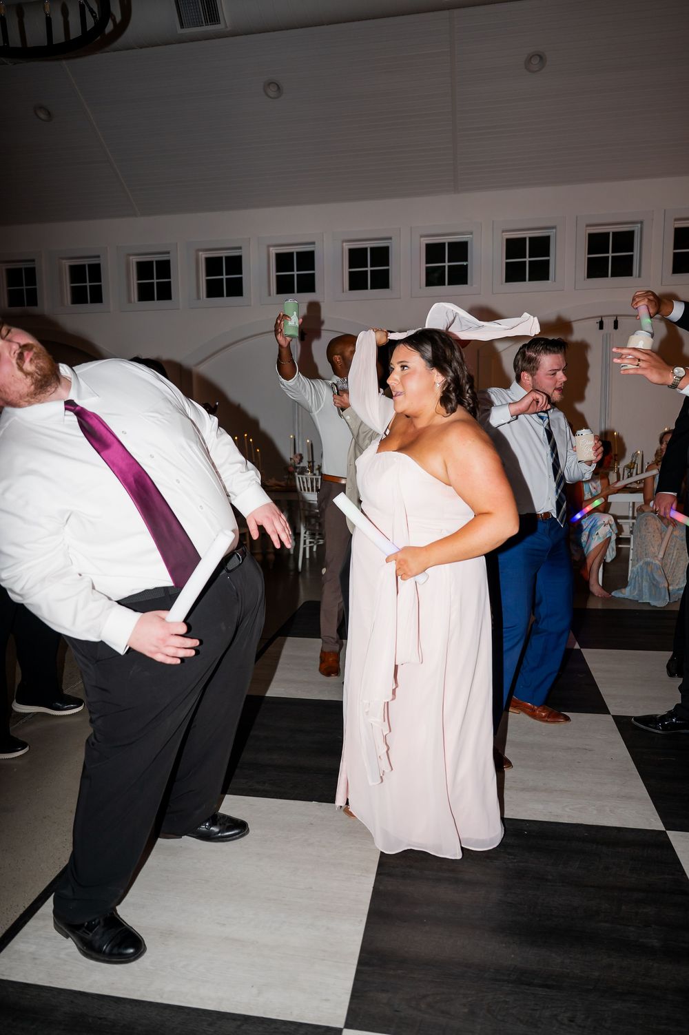 Wedding guests dancing energetically on a black and white checkered dance floor.