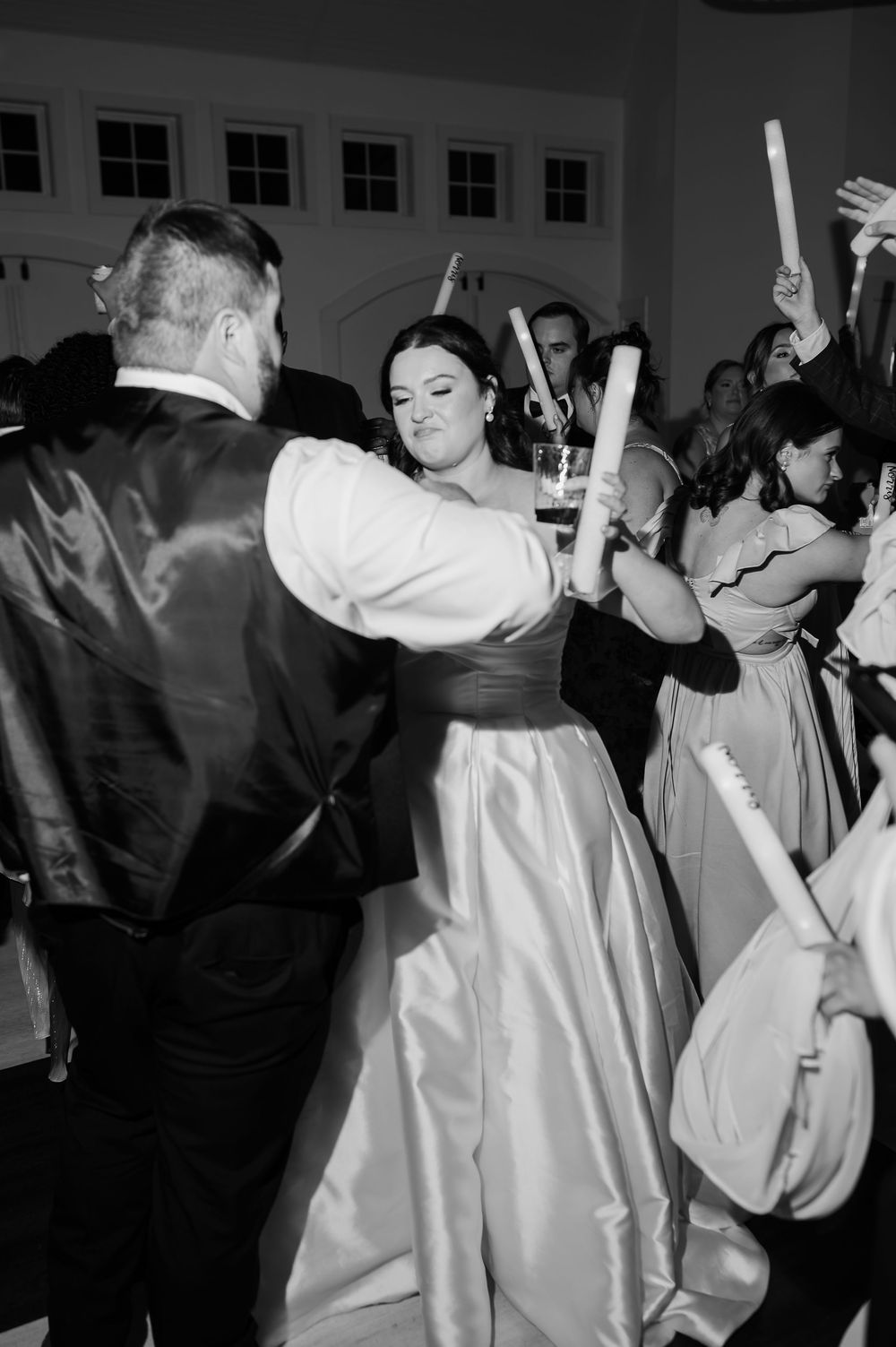 Wedding reception dance party with guests holding light sticks in black and white.