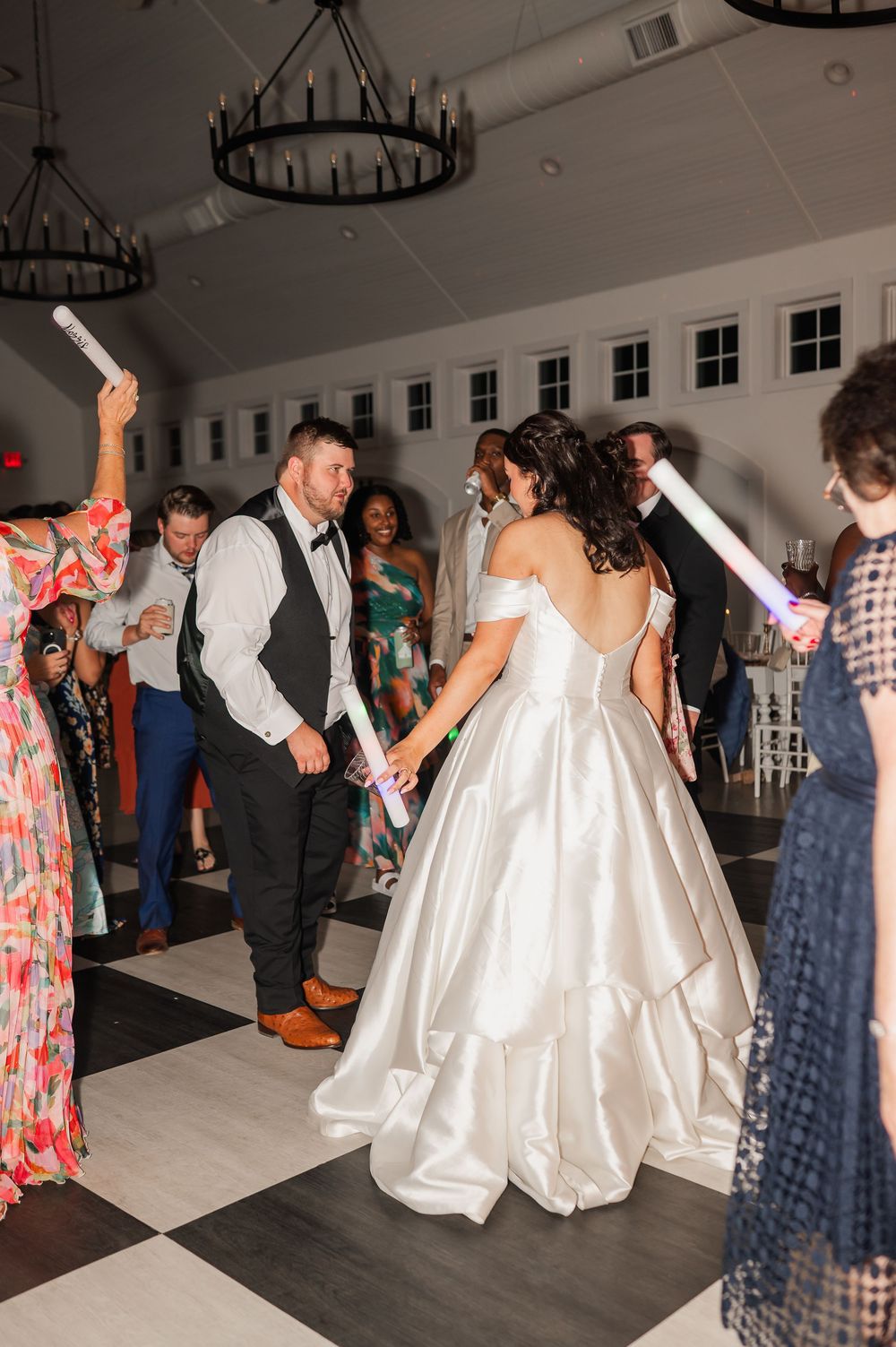 Wedding guests dancing and celebrating on a white dance floor at an indoor reception venue.