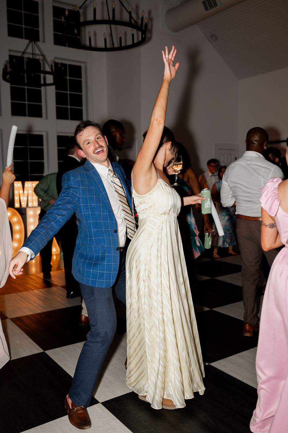 Wedding guests dancing energetically in a reception hall with chandeliers.