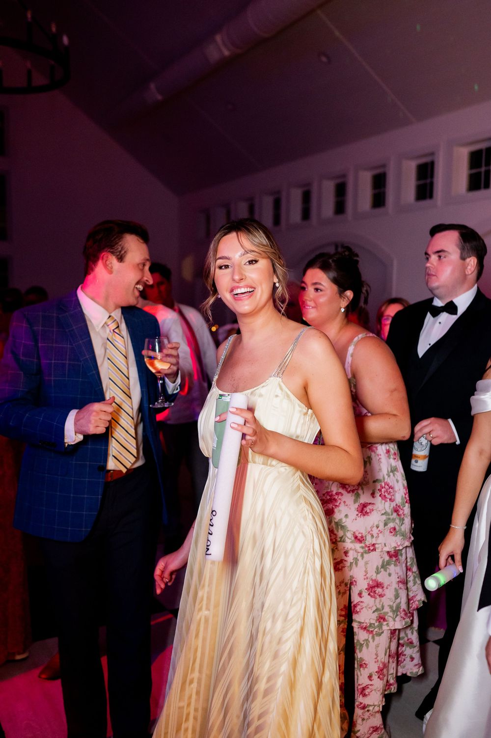 Wedding celebration with guests dancing under purple lighting in an indoor venue.