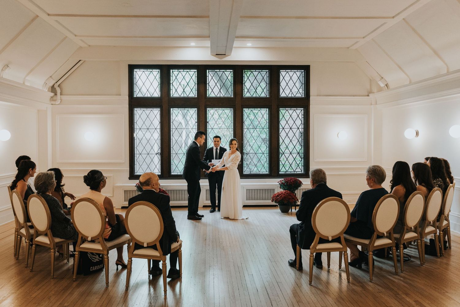 People seated in chairs arranged in rows inside a bright, minimalist room with white walls and hardwood floors.
