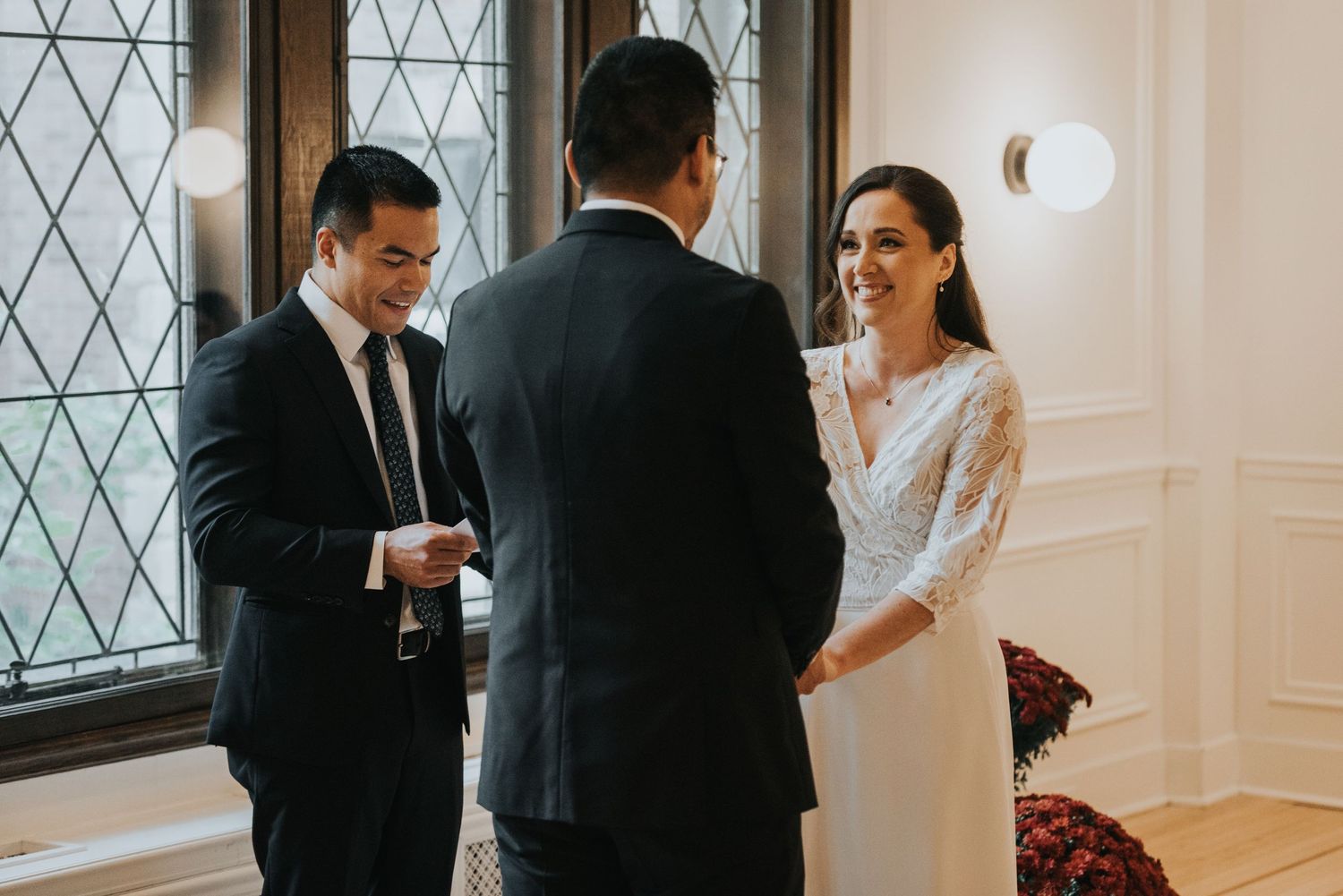 Wedding party laughs together during an elegant indoor celebration with diamond-paned windows in the background.
