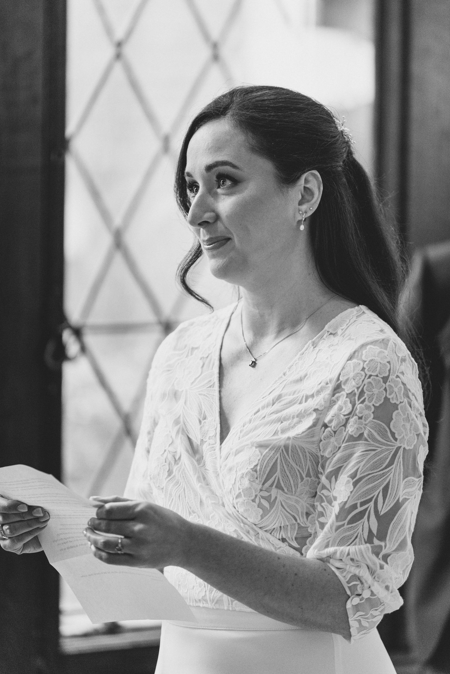 A person in a white lace dress sips from a teacup while standing in an elegant room.