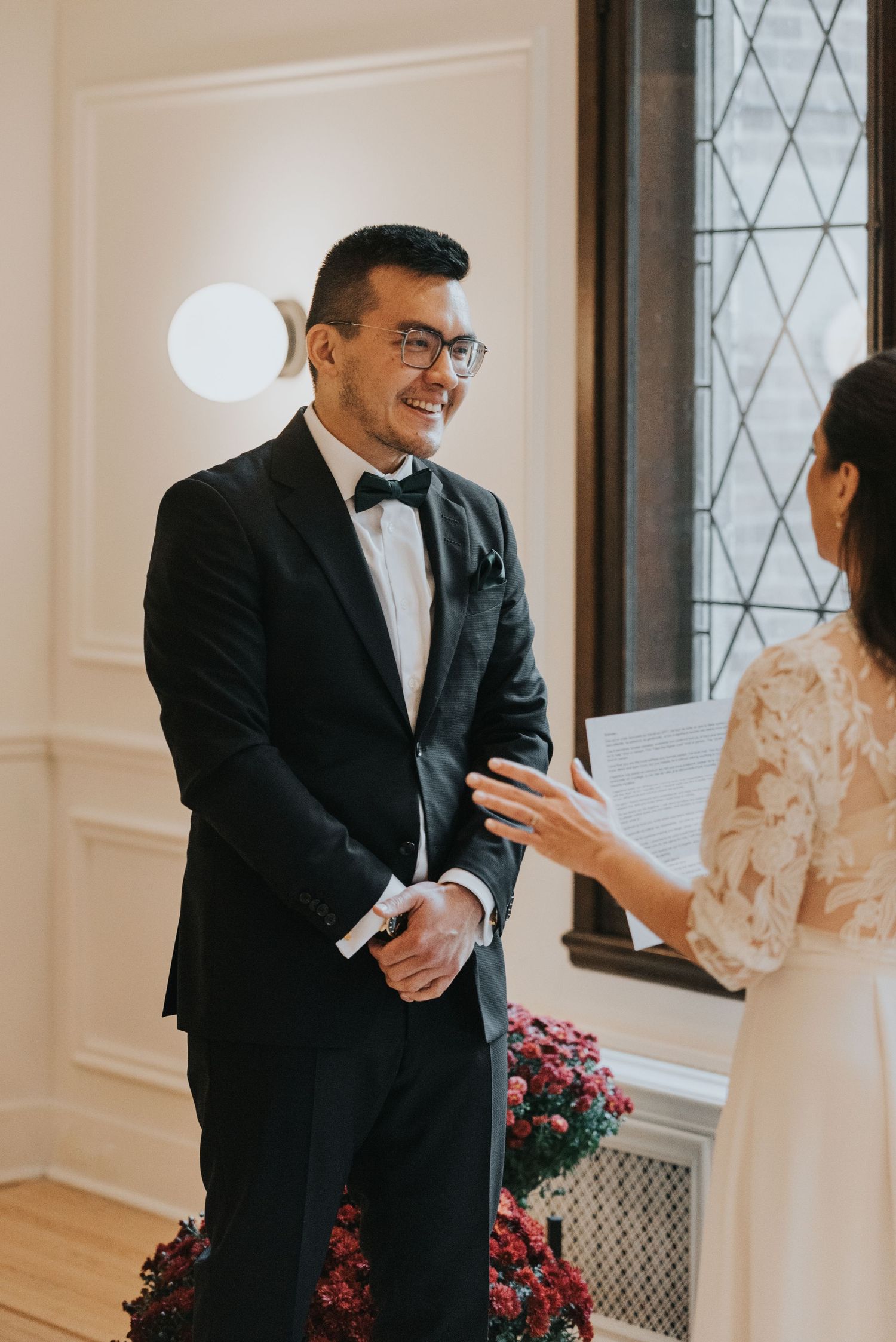 Wedding celebration scene with formal attire and pink floral arrangements in a bright interior space.