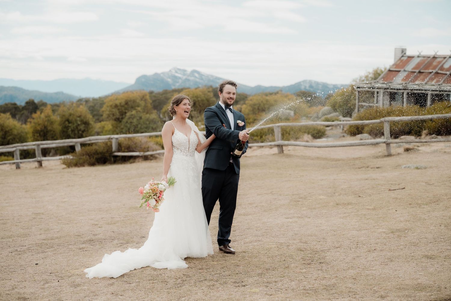 A couple in wedding attire walks together through a scenic desert landscape at sunset at Craigs Hut