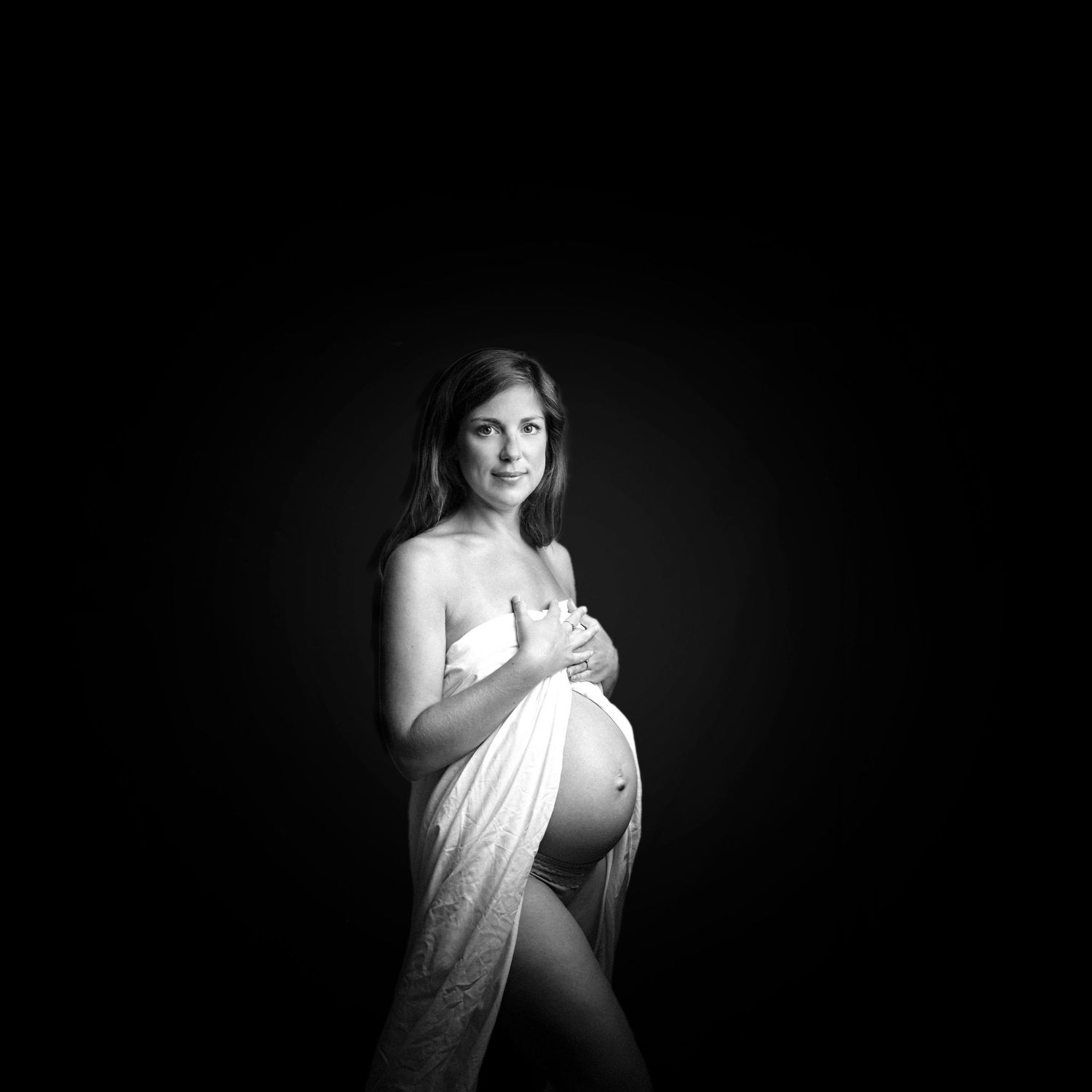 amazing black and white image of a pregnant woman. she has a sheet wrapped around her, with her hands over her chest.
