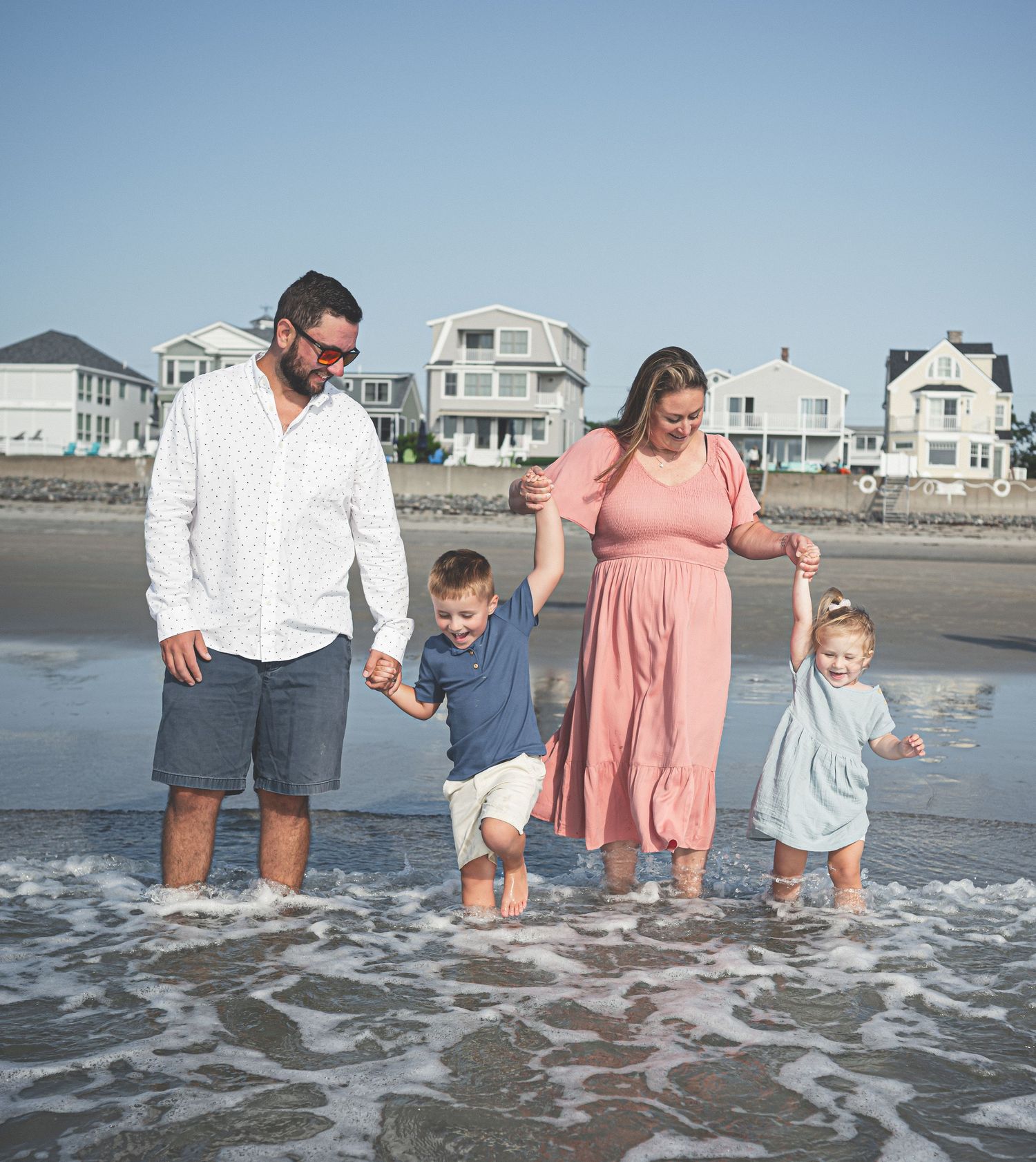 Family photography session at Wells Beach, Maine with a group posing together on a sunny beach with white sand and blue sky