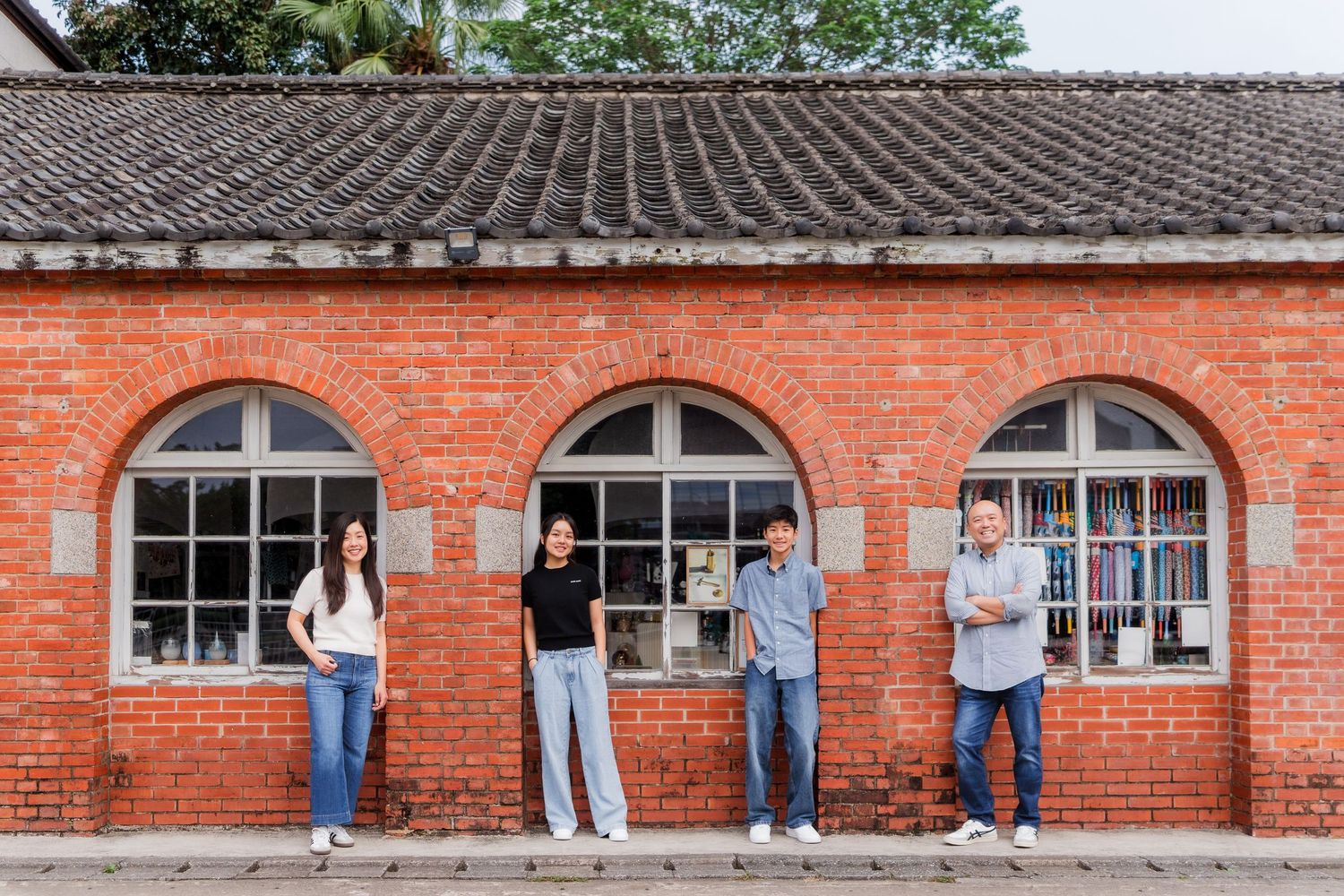 People stand outside a historic red brick building with arched windows while taking photographs of the architecture.