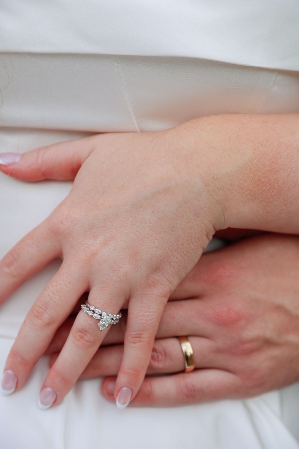 Wedding rings displayed on hands with a diamond engagement ring and gold wedding band against white fabric.