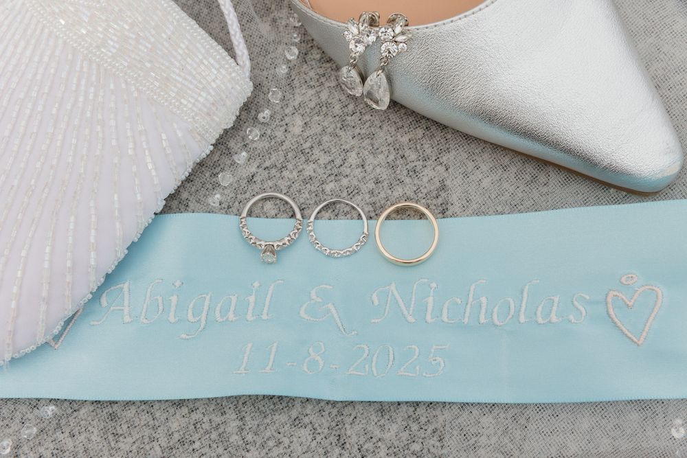 A light blue wedding garter with delicate lace detail and silver embellishments lies on a textured surface.