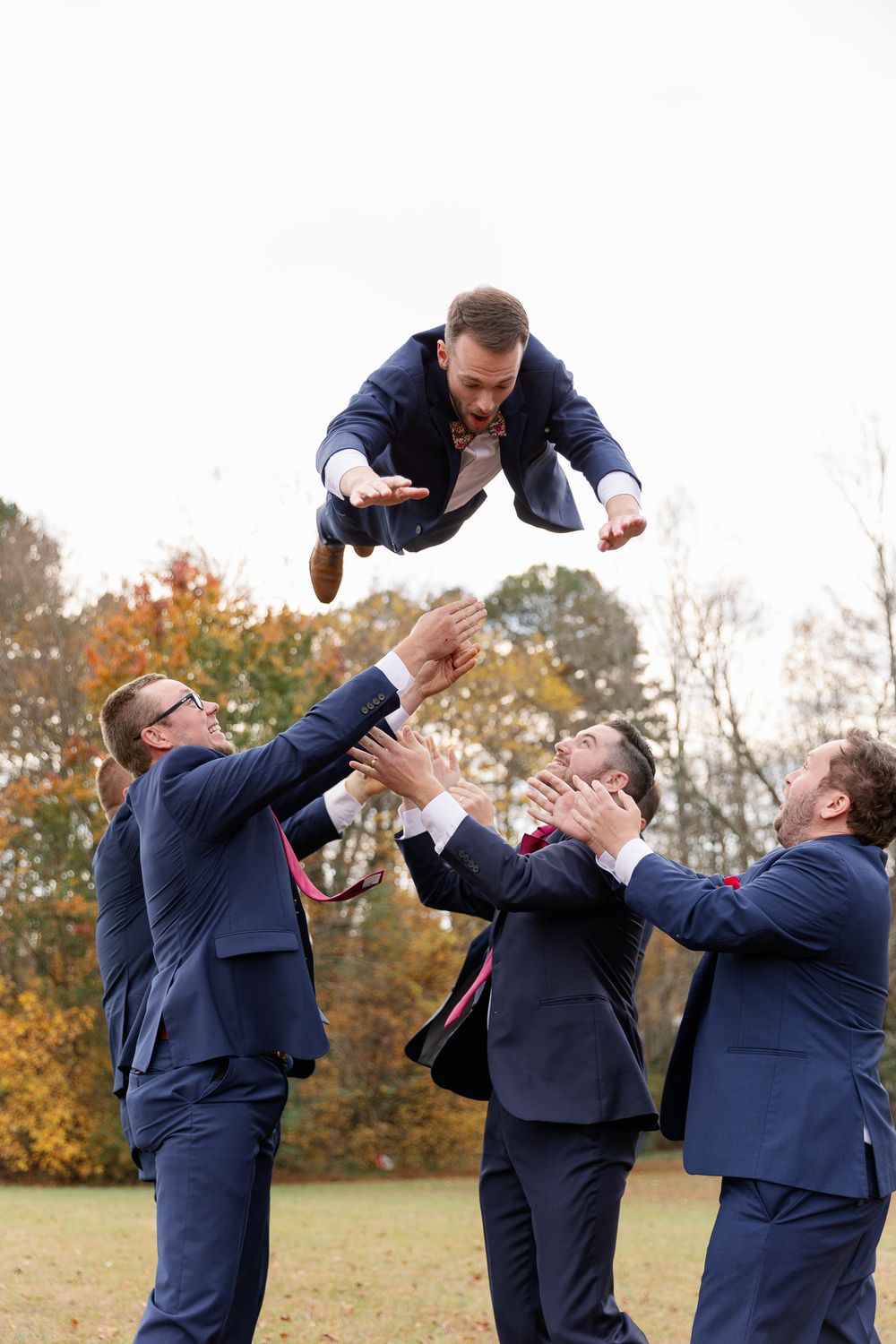 Two groomsmen in navy suits playfully stage a mock fight sequence in a series of outdoor photos.