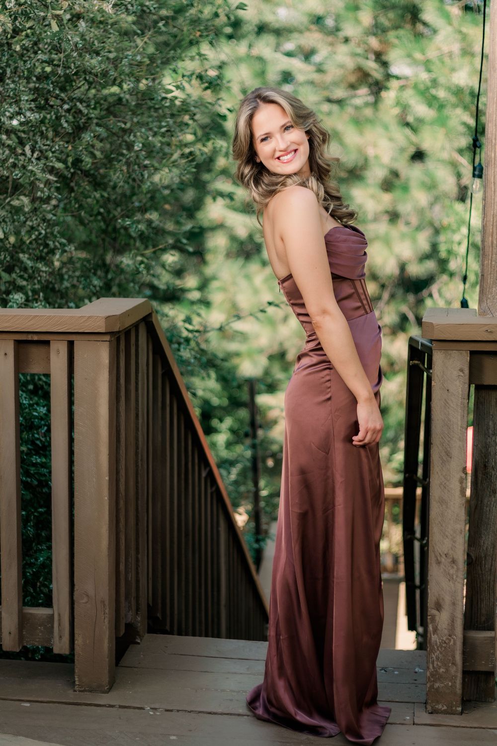 A sequence of photos shows someone in a burgundy dress posing playfully on a wooden deck surrounded by greenery.