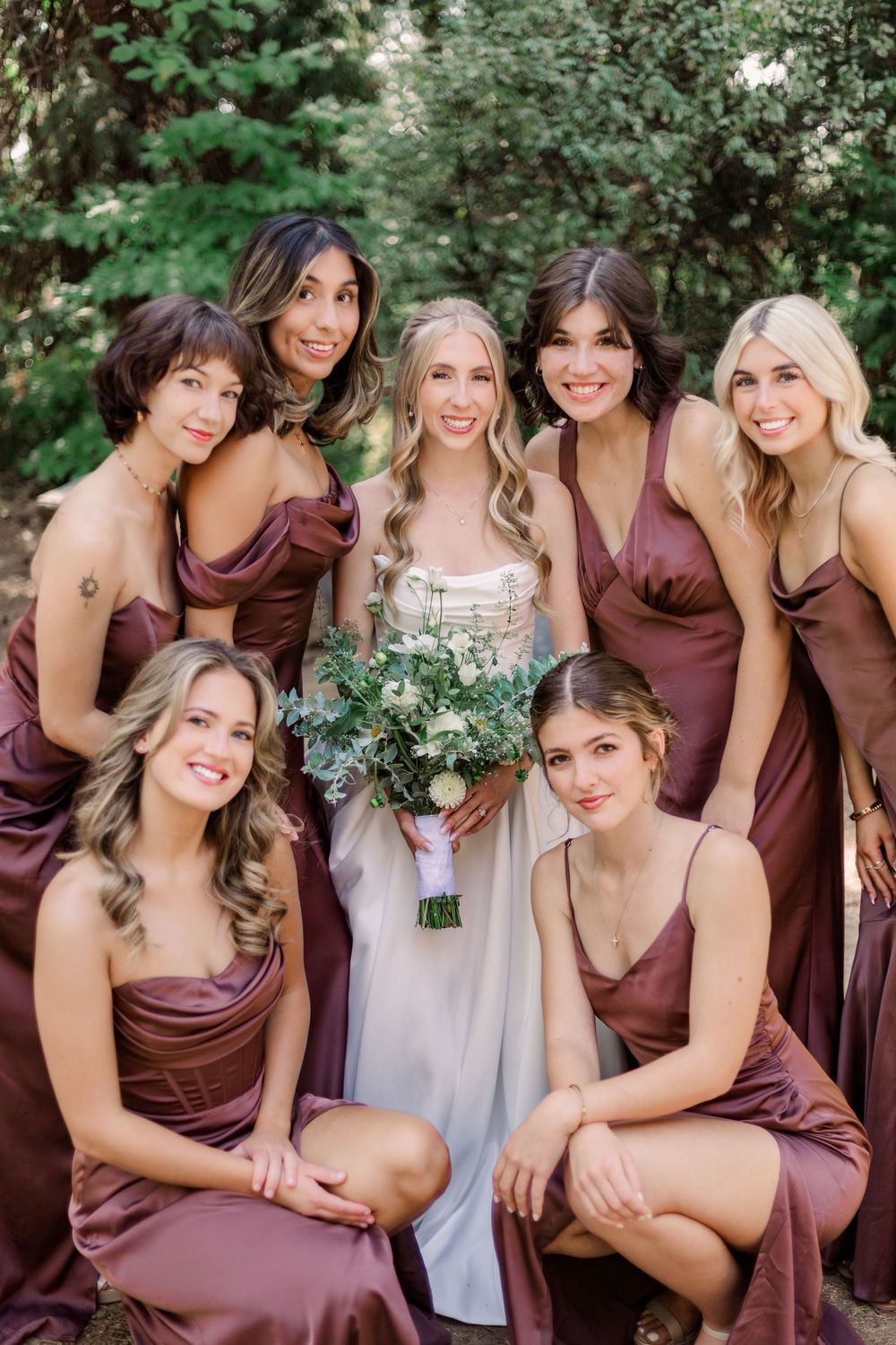 Bridesmaids in burgundy dresses gather together for group photos in an outdoor garden setting.