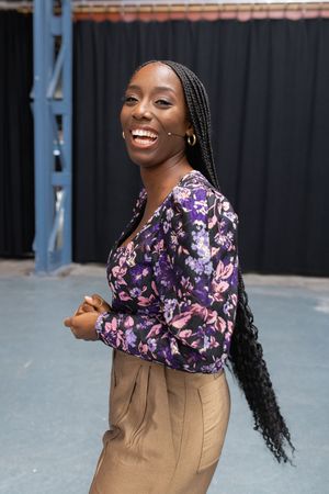 Woman in floral top and tan skirt posing confidently against dark backdrop.