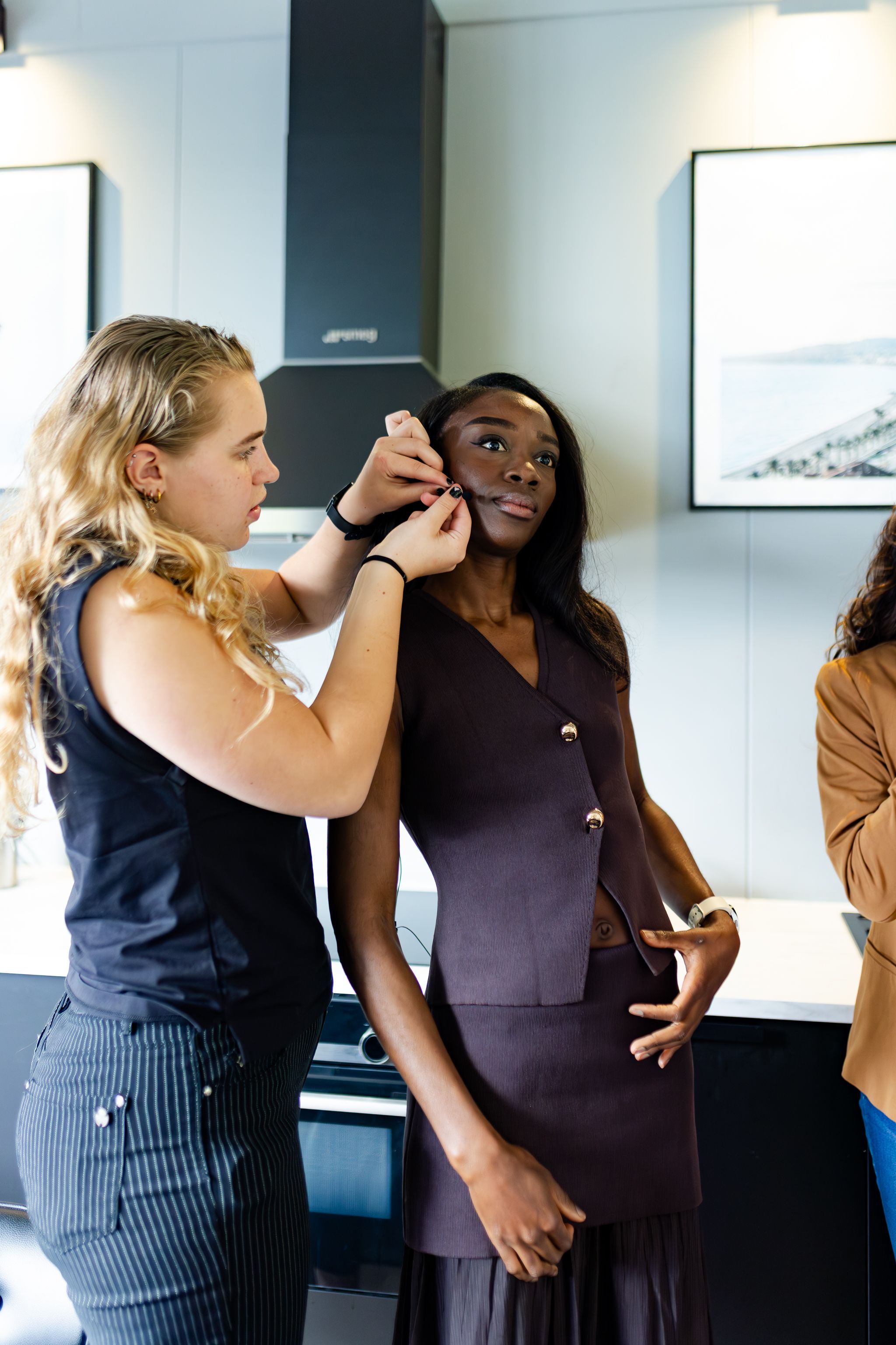 A makeup artist applies cosmetics to a model wearing a dark dress during a professional photoshoot.