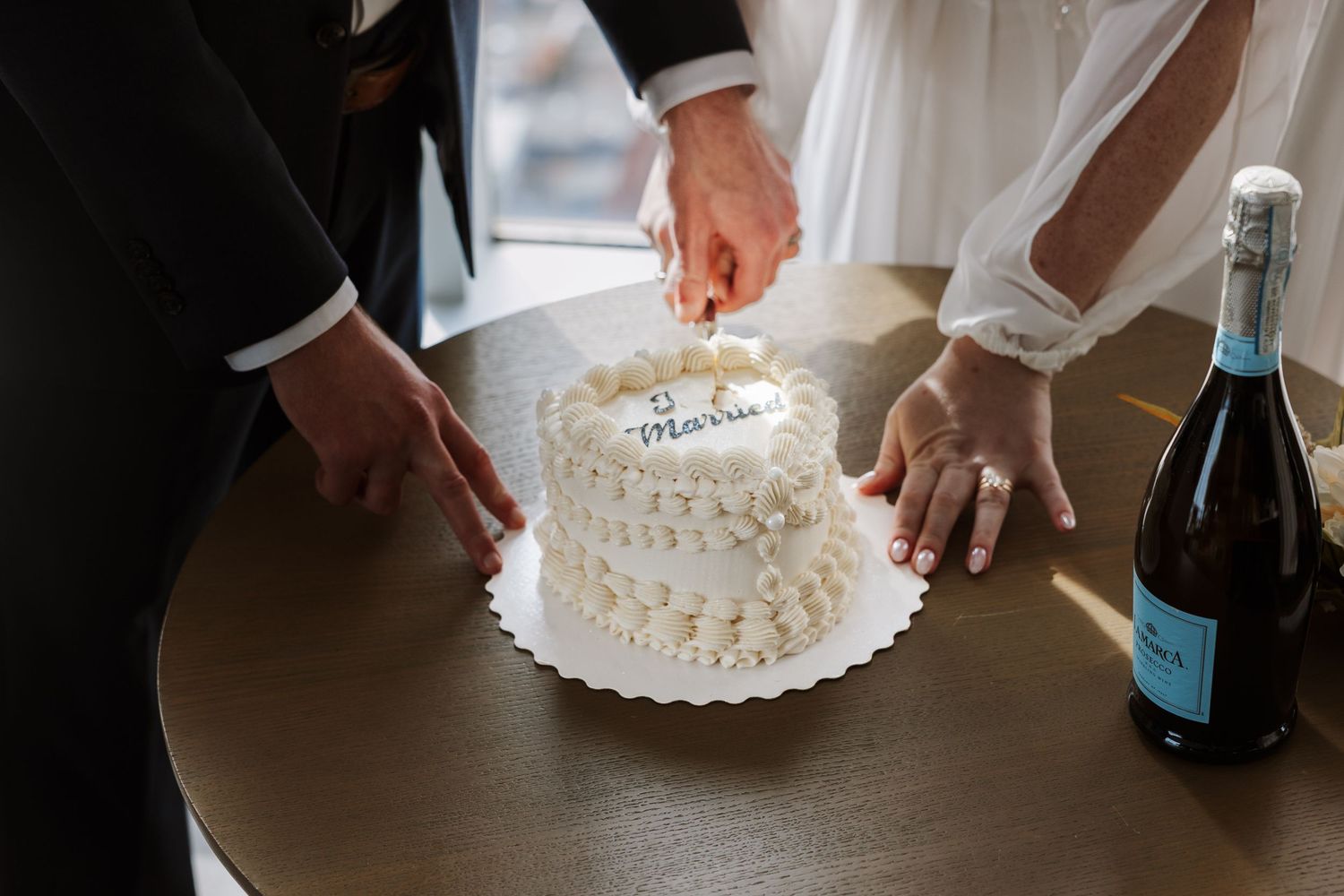 A couple cutting into a white wedding cake together during their reception celebration.