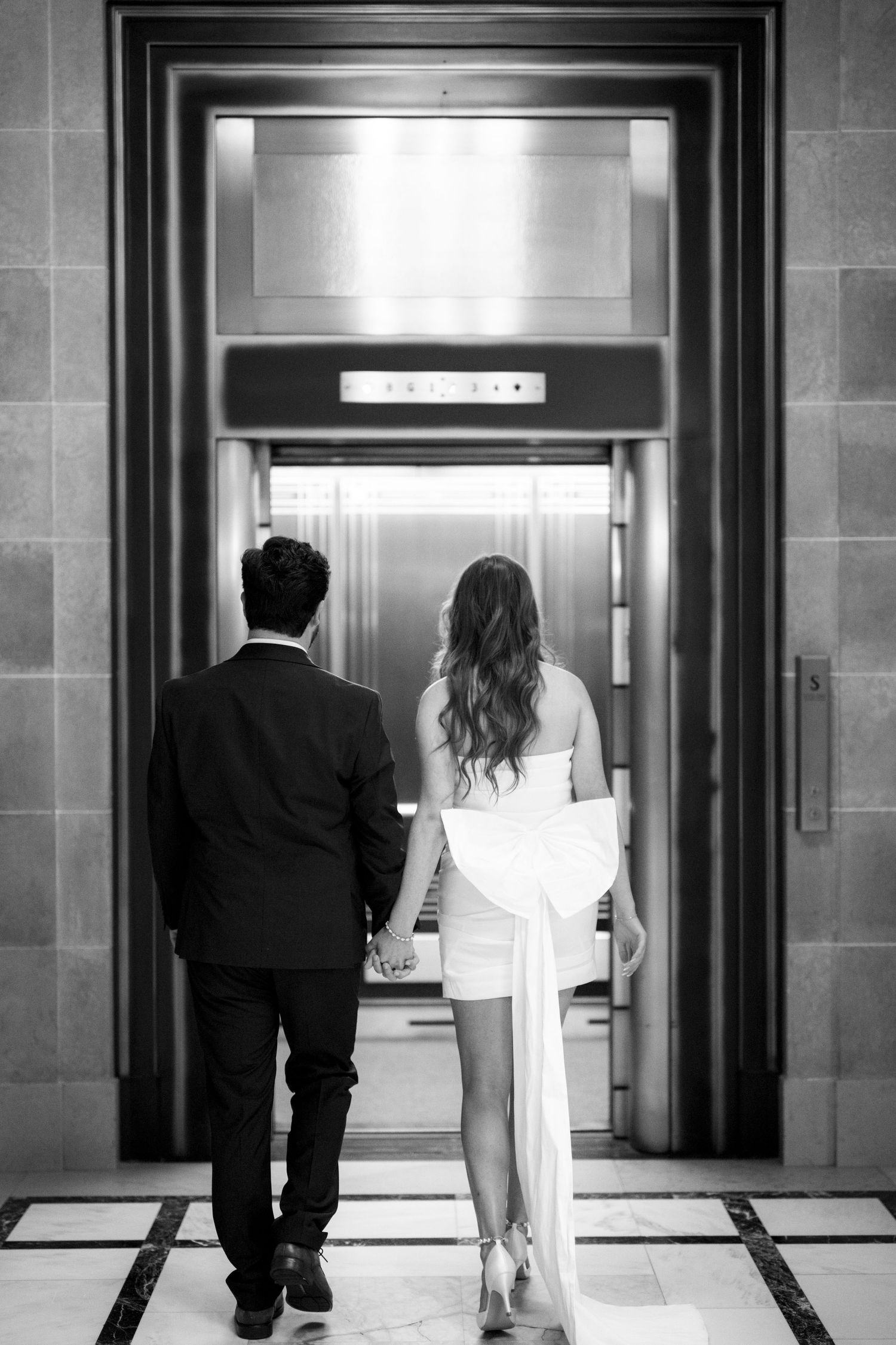 A couple in formal wear approaches an elegant elevator entrance.