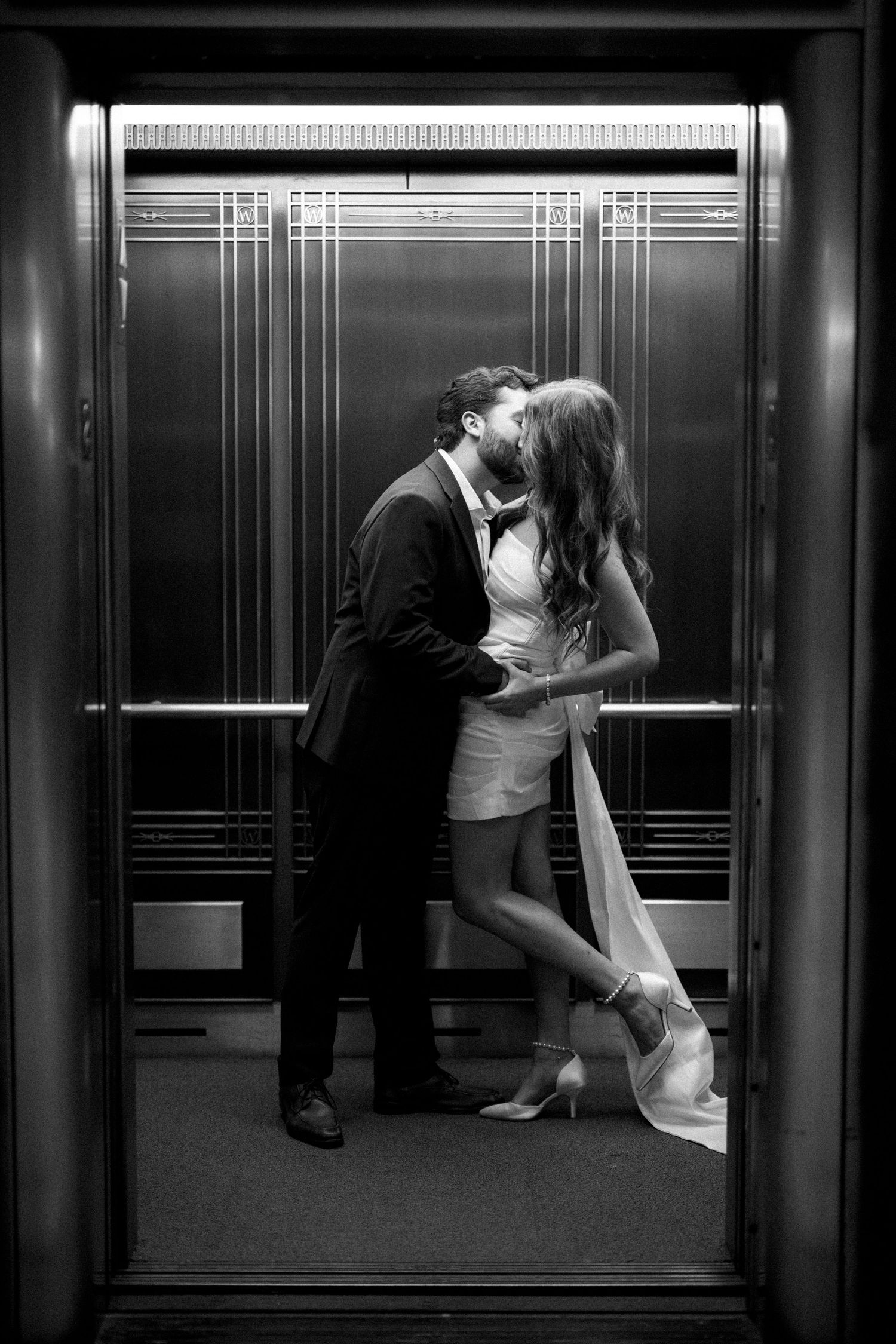 An intimate black and white moment captured between a couple in an art deco elevator.