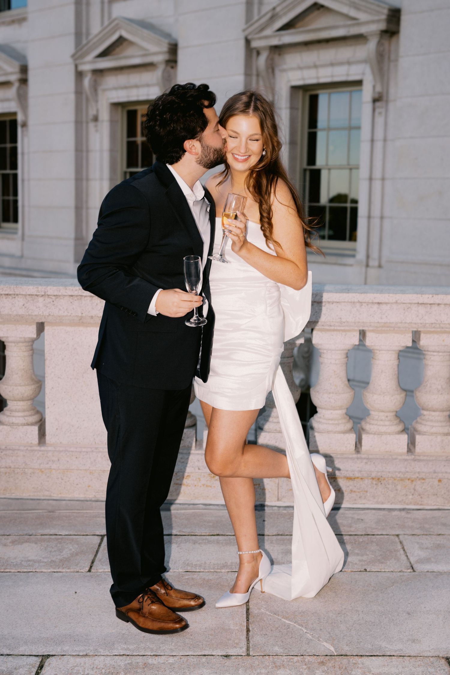 Romantic couple sharing an intimate moment while holding champagne glasses on marble terrace.