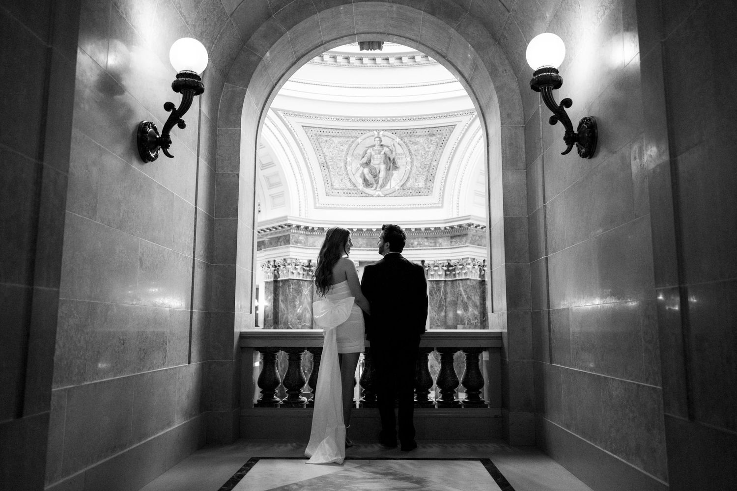 A silhouetted couple stands in an arched hallway with classical architectural details.