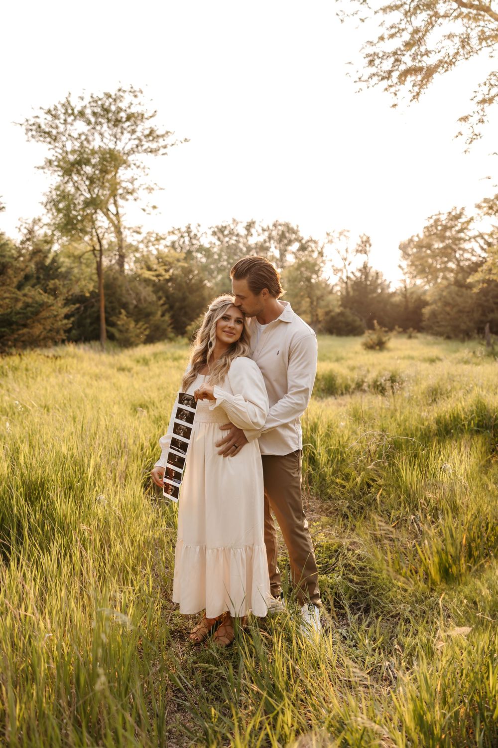 Expectant couple sharing intimate moment in golden field at sunset.