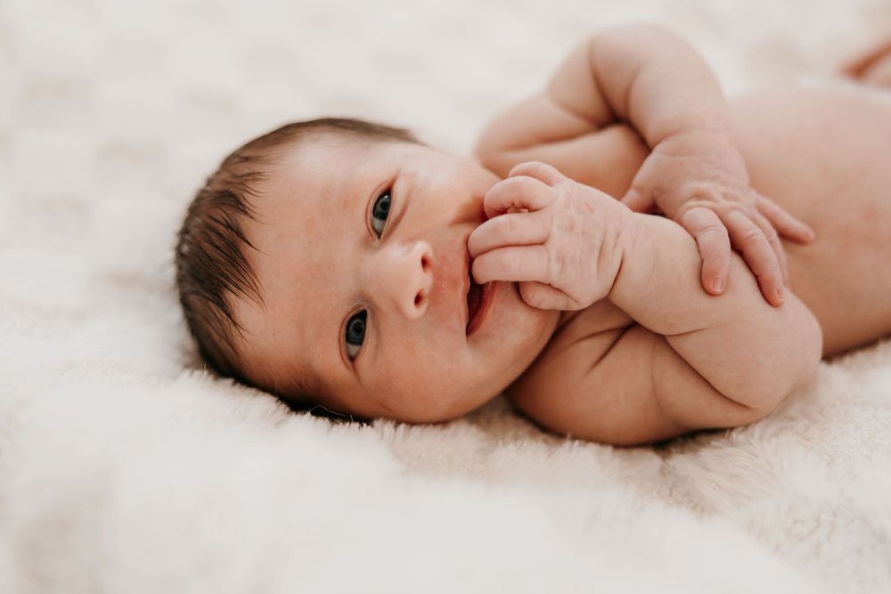 Newborn baby in natural light laying on white textured surface.