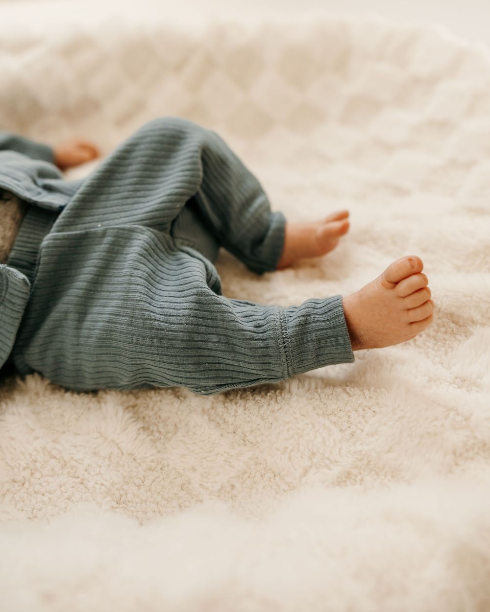 Close-up of tiny baby feet in soft gray ribbed clothing on cream fabric.