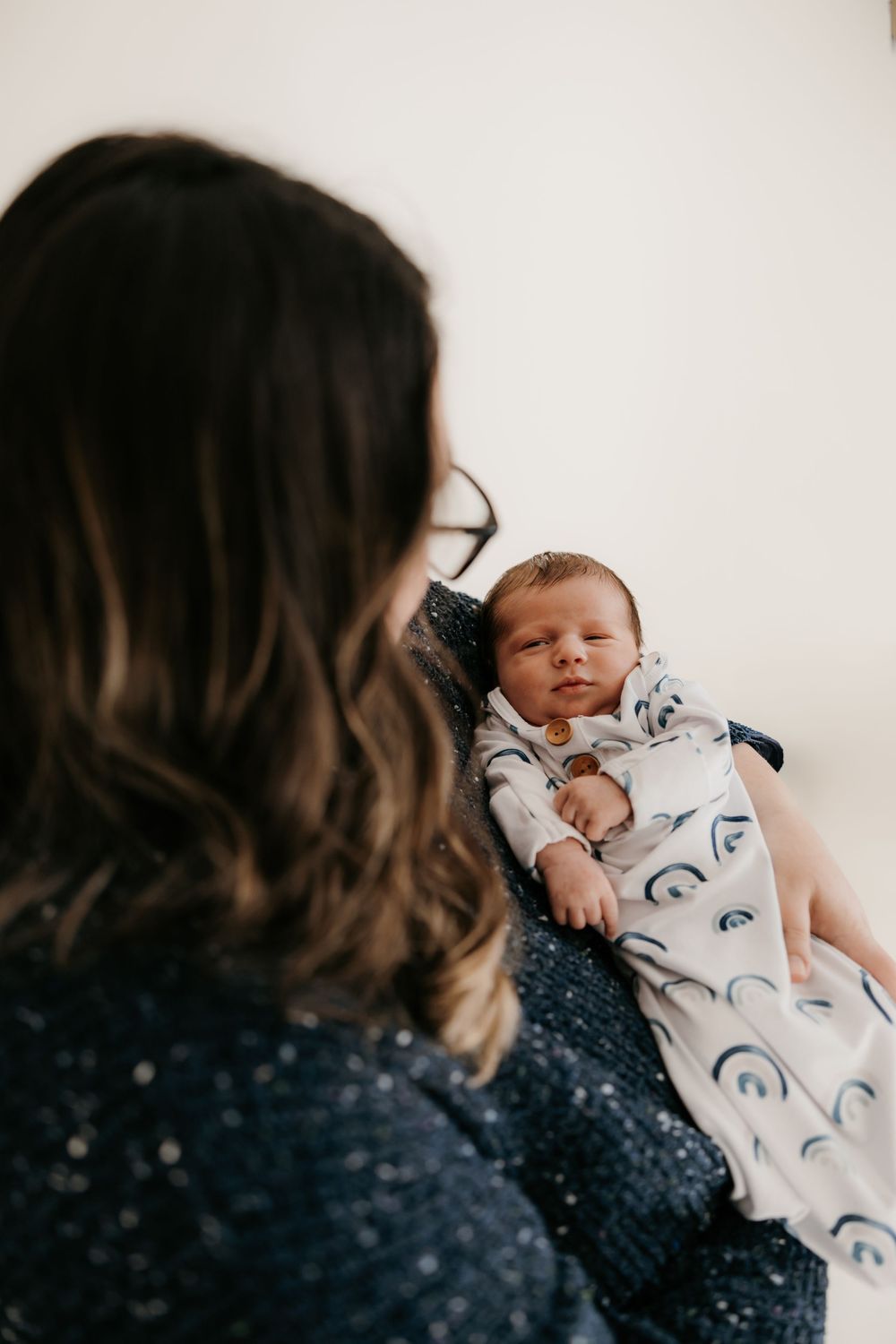 Newborn in patterned onesie lying peacefully on soft blanket.