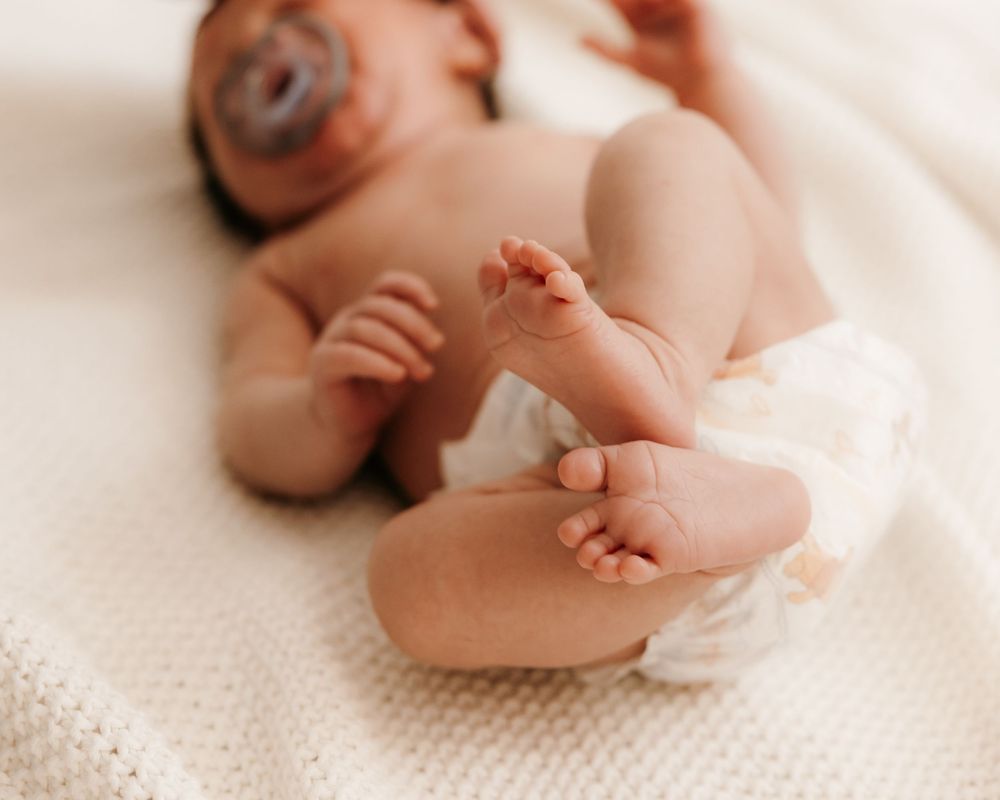 Tiny newborn baby feet against soft white textured fabric background.