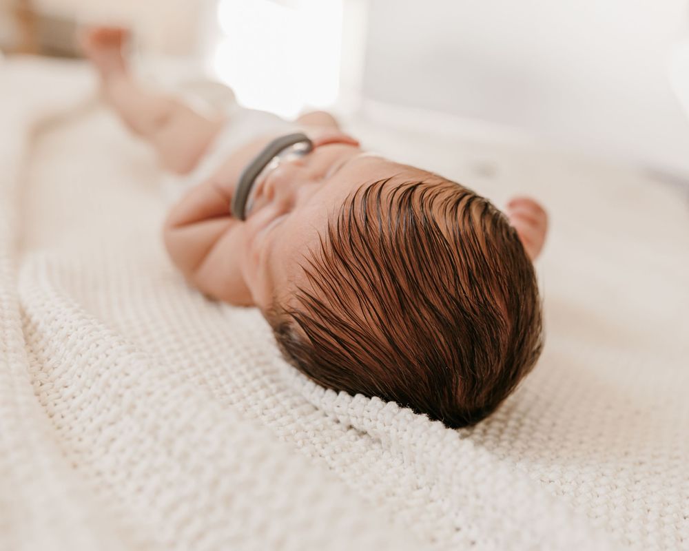 Side view profile of sleeping newborn baby on white knit blanket.