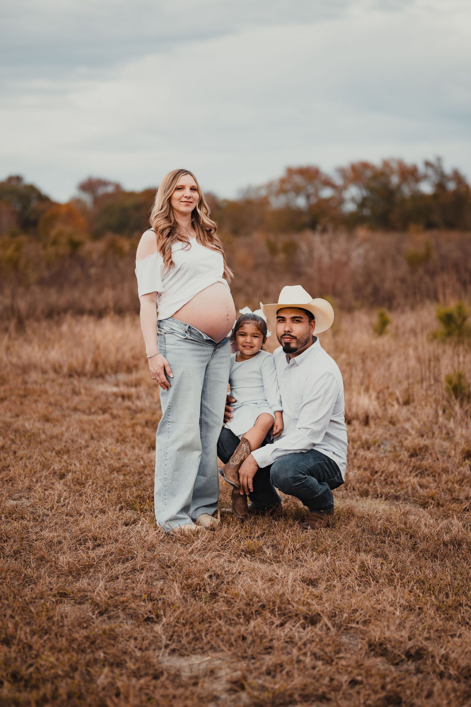 A family poses together in a rustic autumn field during a maternity photo session at sunset.