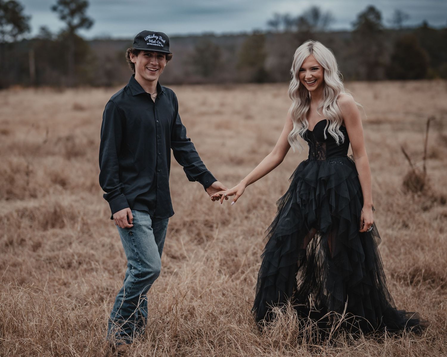 Stylish couple walking through a field at dusk holding hands and smiling.