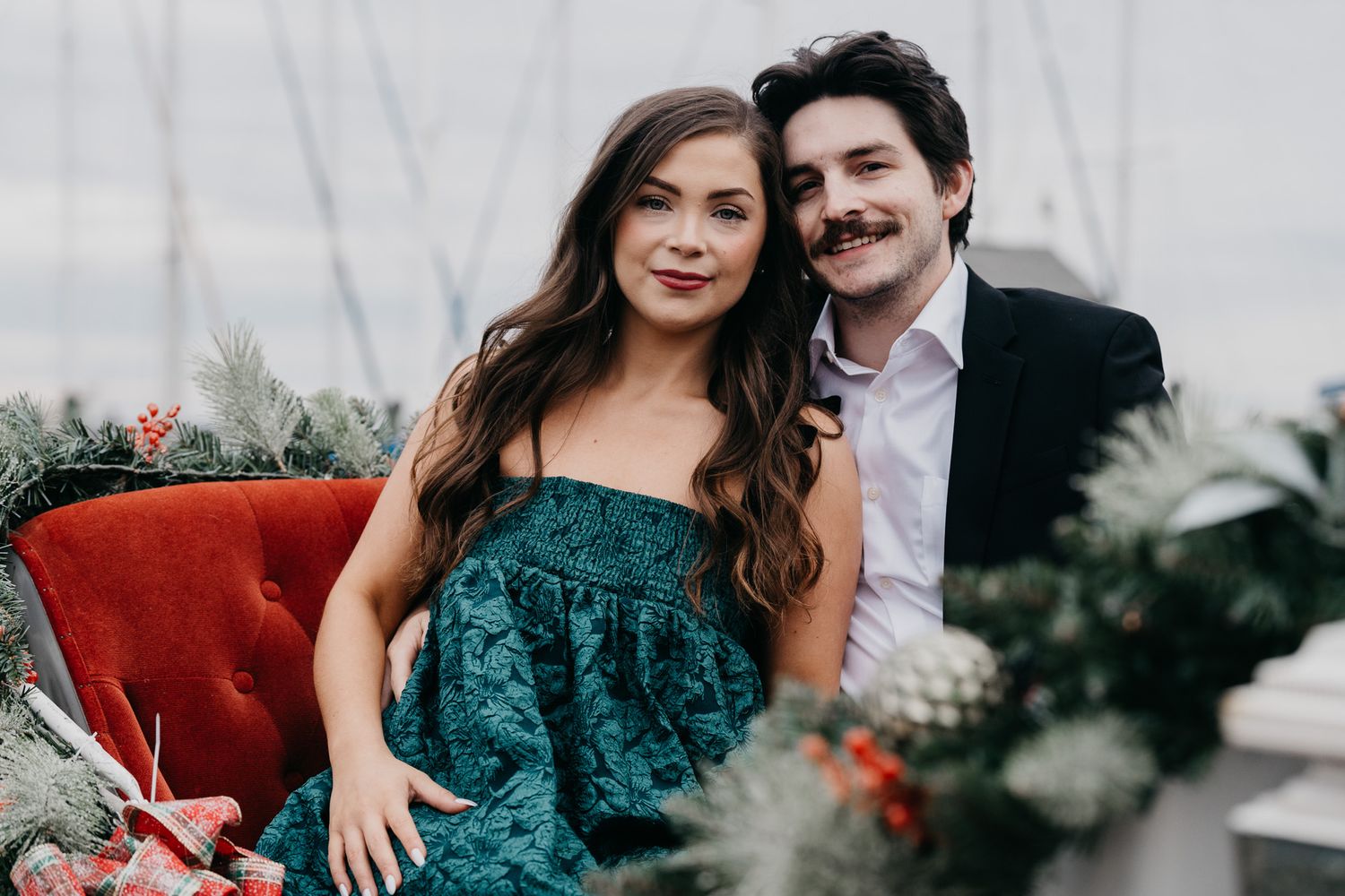 Couple in formal wear seated on red furniture during an elegant photo session.