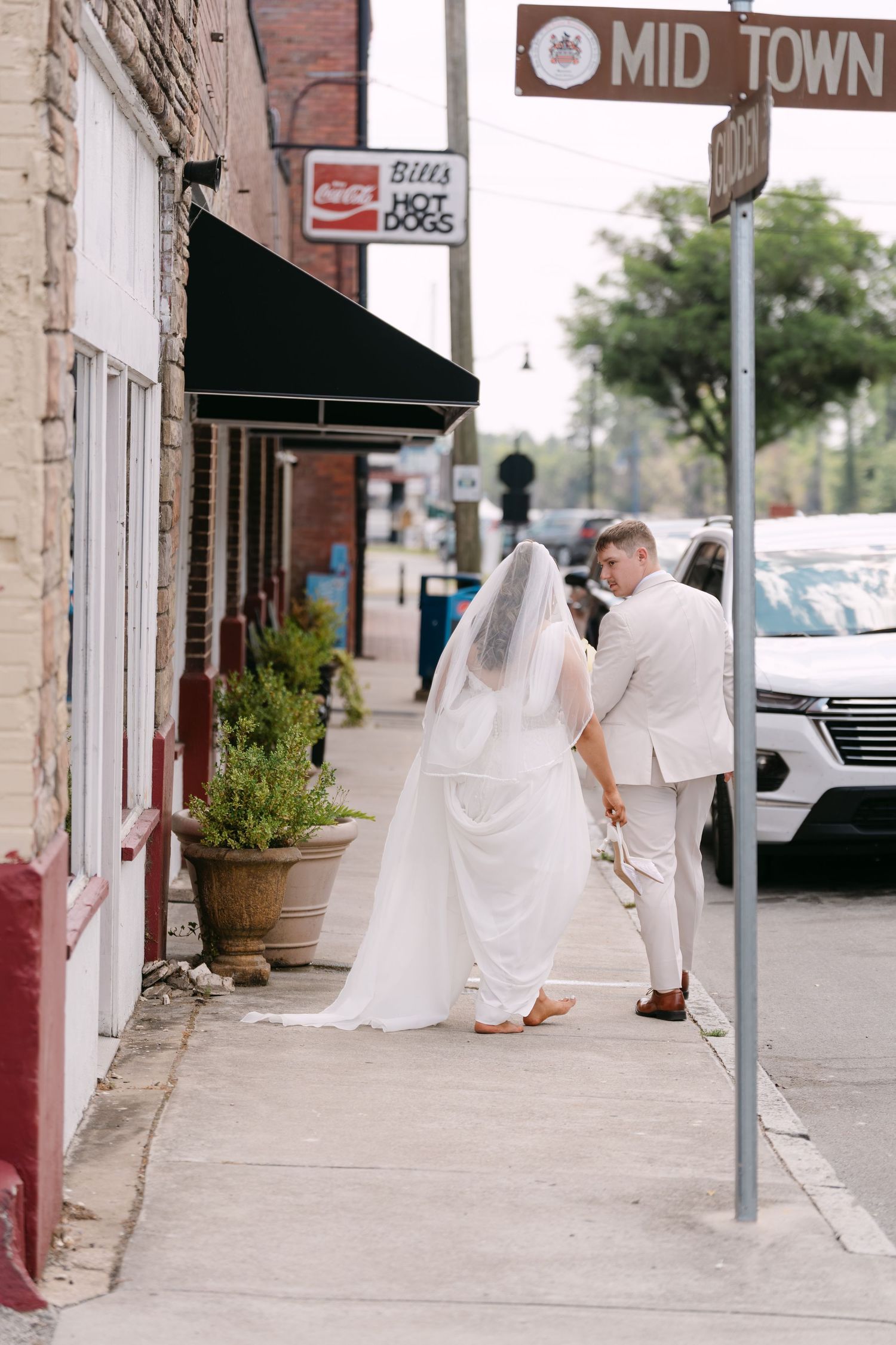 Bride and groom walking hand in hand on a sidewalk in Midtown, bride wearing a white gown with veil.