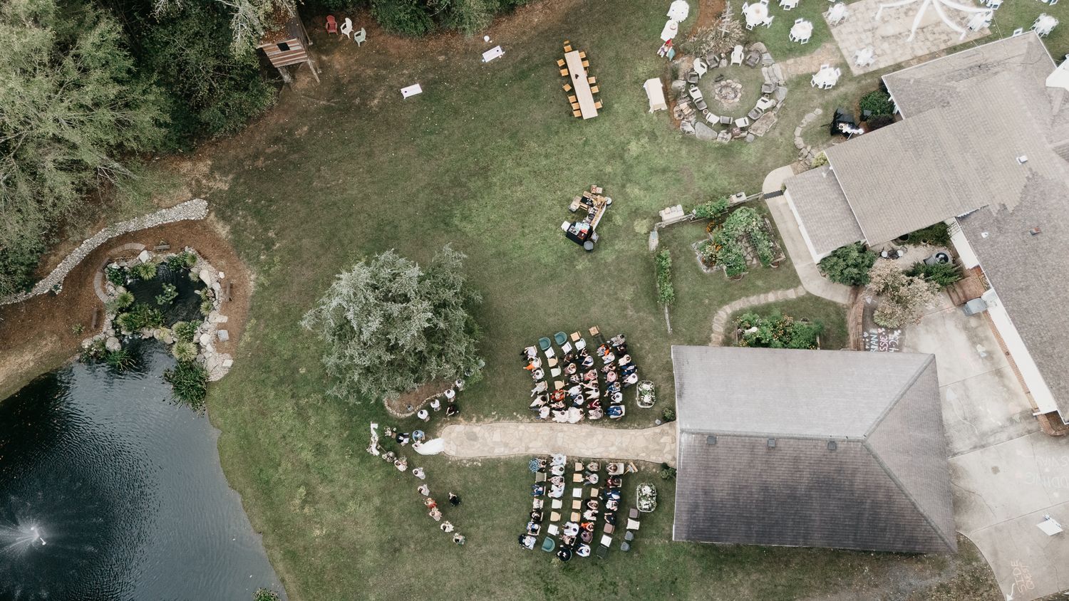 Aerial view of an outdoor event setup with rows of chairs beside a building and pond.