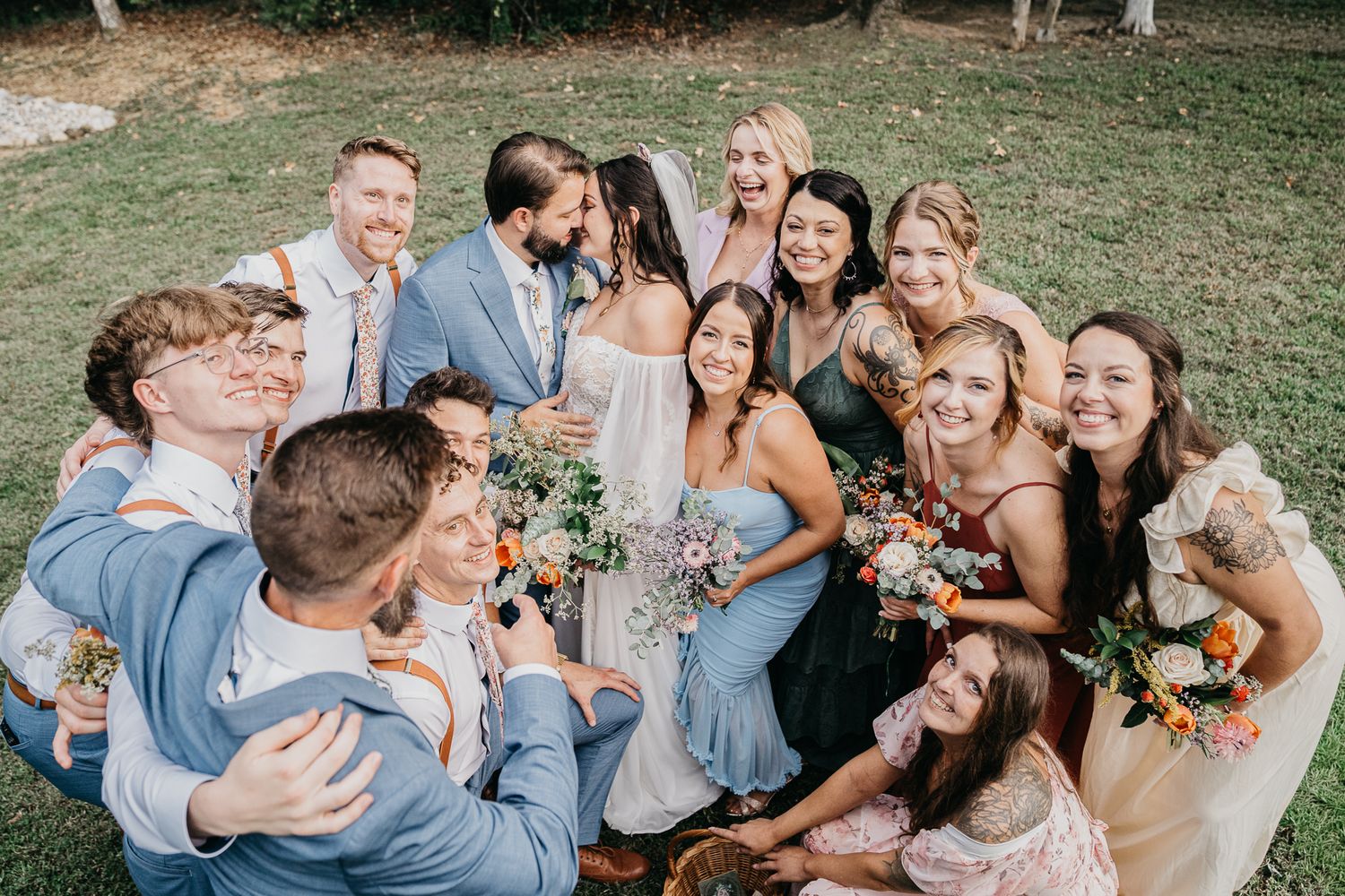 Wedding party in light blue and neutral colors laughs together during candid outdoor photo session.
