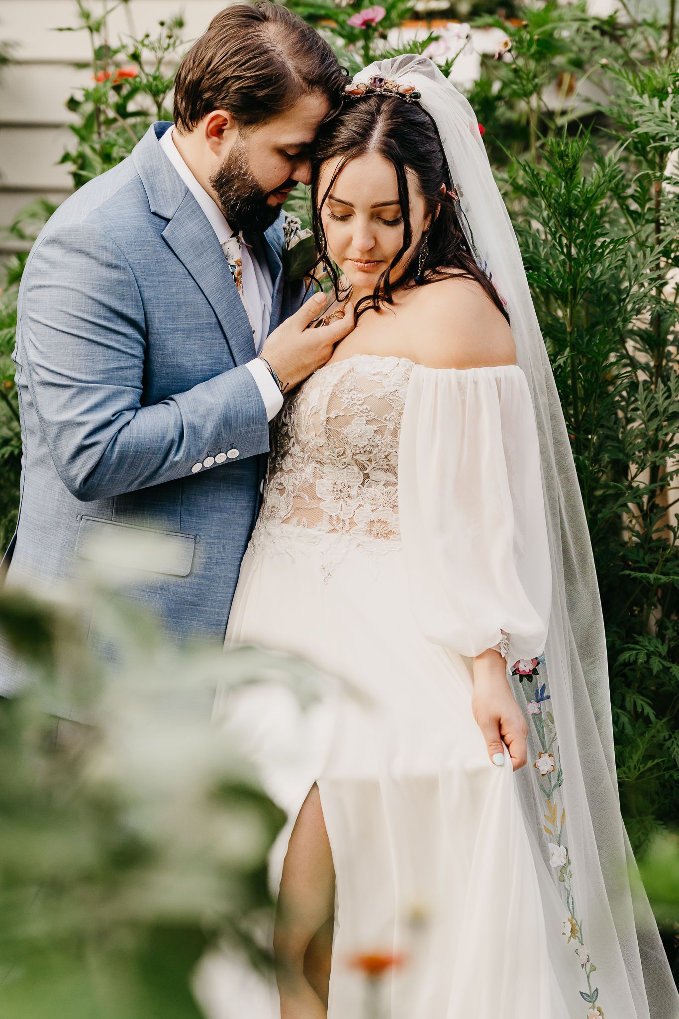 Romantic wedding couple embraces in a lush garden setting with soft natural lighting and flowing white veil.