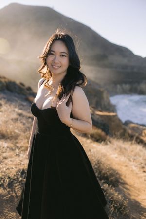 A black dress contrasts beautifully against a misty coastal mountainside during golden hour lighting.