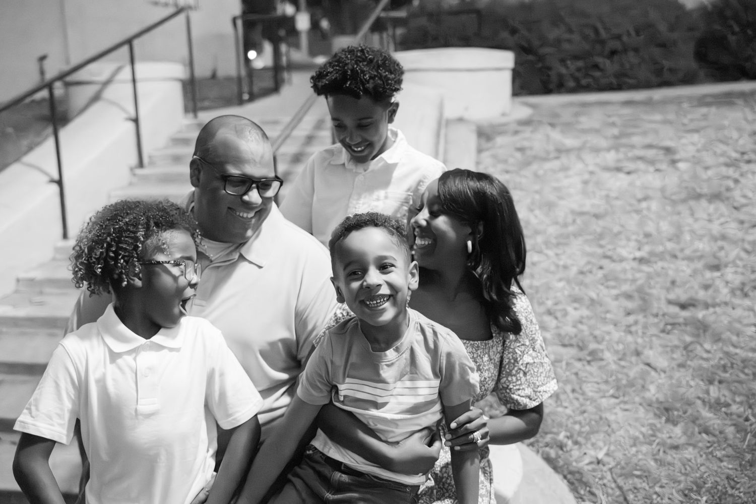 A candid black and white photo shows a joyful family group sitting together outdoors and laughing.