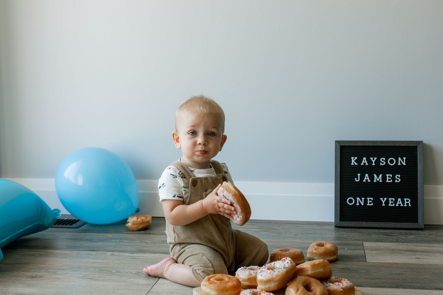 One year birthday setup with blue balloons, letter board, and donuts surrounding a toddler.