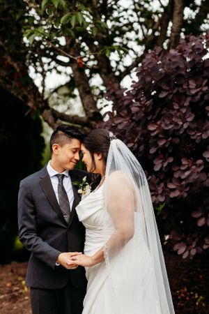 A romantic wedding moment captured outdoors against purple foliage and greenery.
