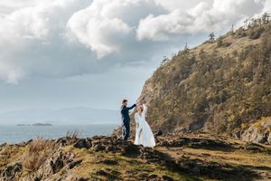 Two silhouettes stand together on a dramatic coastal cliff overlooking the ocean under cloudy skies.