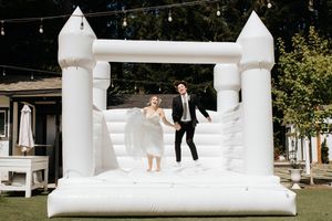 A couple jumping together on an all-white bouncy castle at an outdoor event venue.