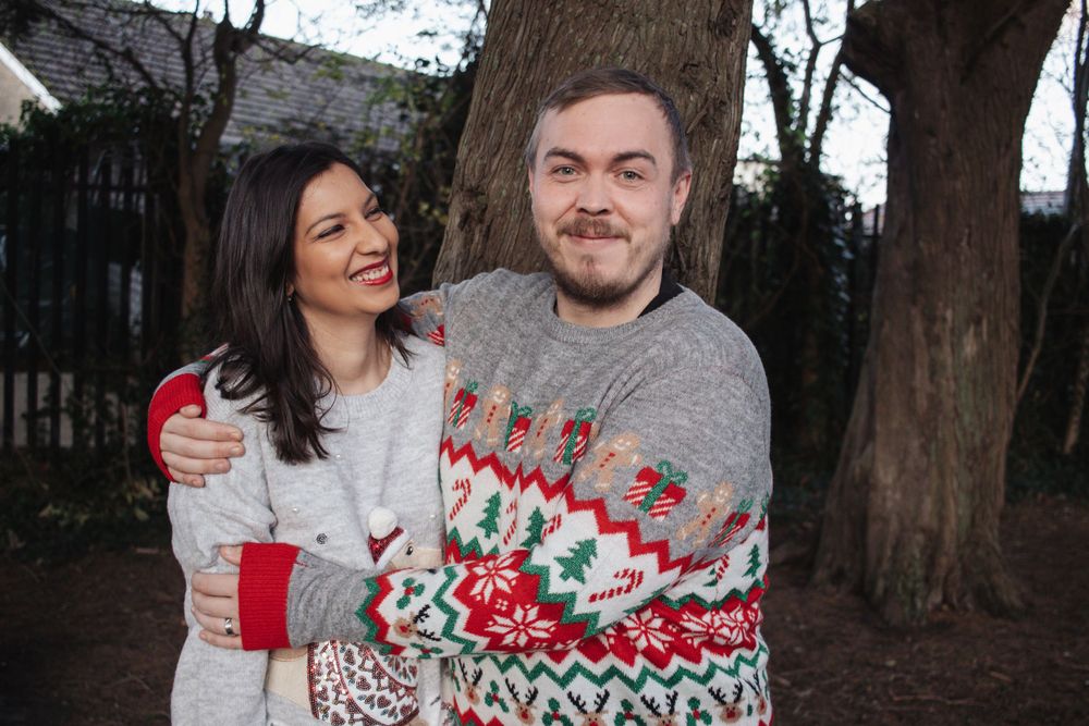 Two people wearing winter sweaters standing outdoors near trees.
