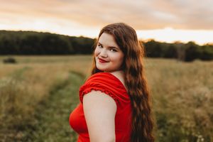 senior girl red shirt red lips brown curly hair sunset golden hour looking over shoulder