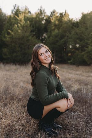 senior girl squatting black skirt black boots green sweater