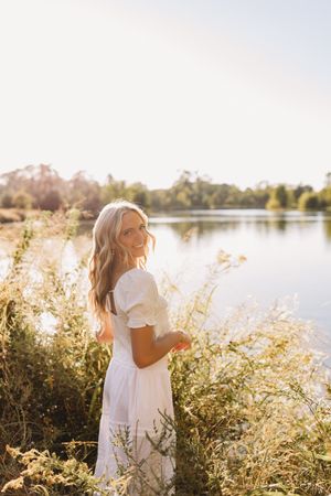 senior girl golden hour white dress lake and tall grass