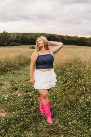 senior girl white skirt blue jean top with hot pink boots in a field